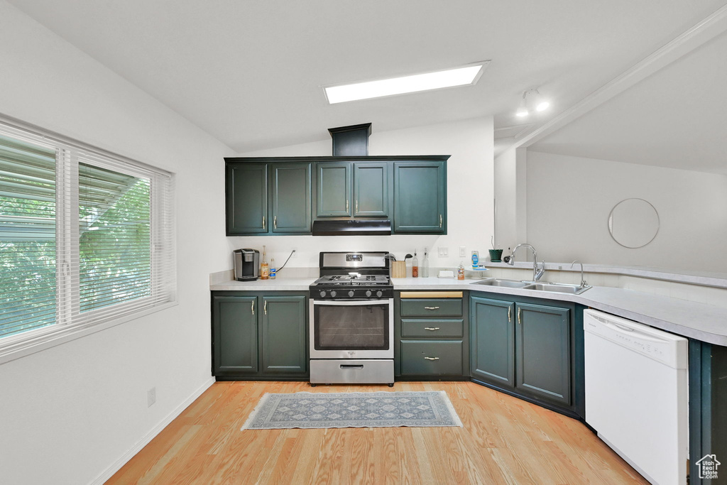 Kitchen with gas stove, dishwasher, under cabinet range hood, light wood-style flooring, and lofted ceiling