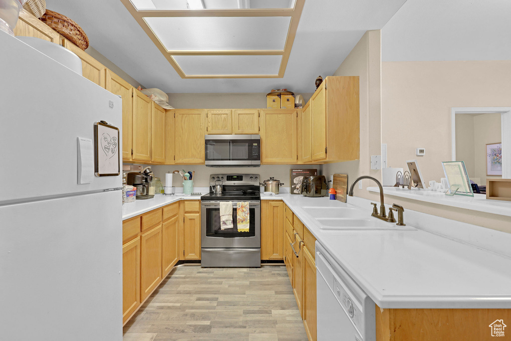 Kitchen with appliances with stainless steel finishes, light brown cabinetry, light wood-style floors, a peninsula, and light countertops