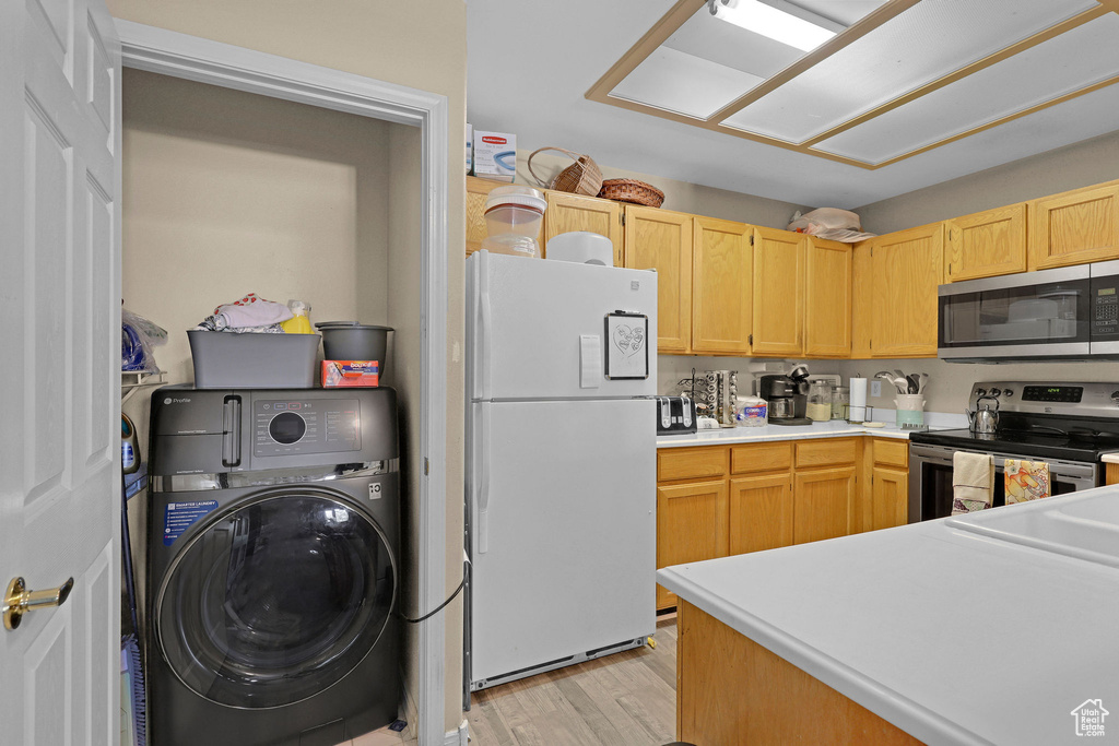 Kitchen featuring stainless steel appliances, washer / dryer, light wood-style floors, light countertops, and light brown cabinetry