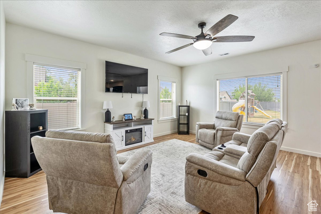 Living area featuring light wood-style floors, ceiling fan, a textured ceiling, and a glass covered fireplace