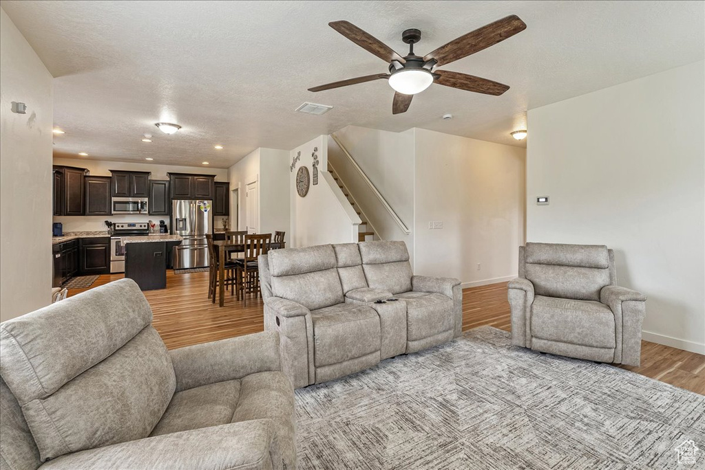 Living room with light wood-style flooring, a ceiling fan, stairs, and recessed lighting