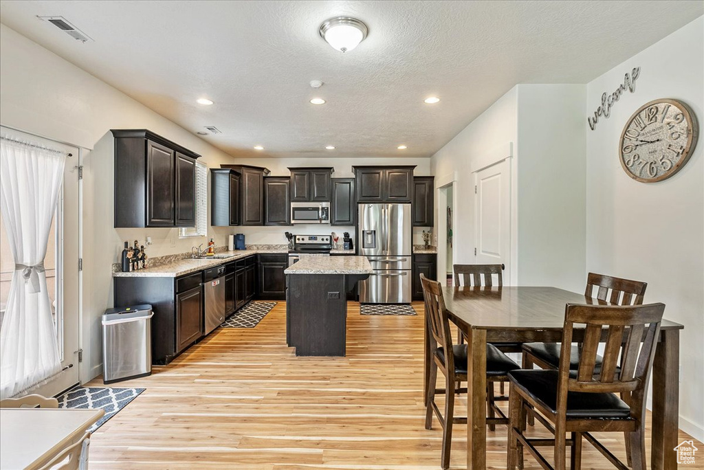 Kitchen with appliances with stainless steel finishes, light wood-style flooring, a center island, recessed lighting, and a textured ceiling