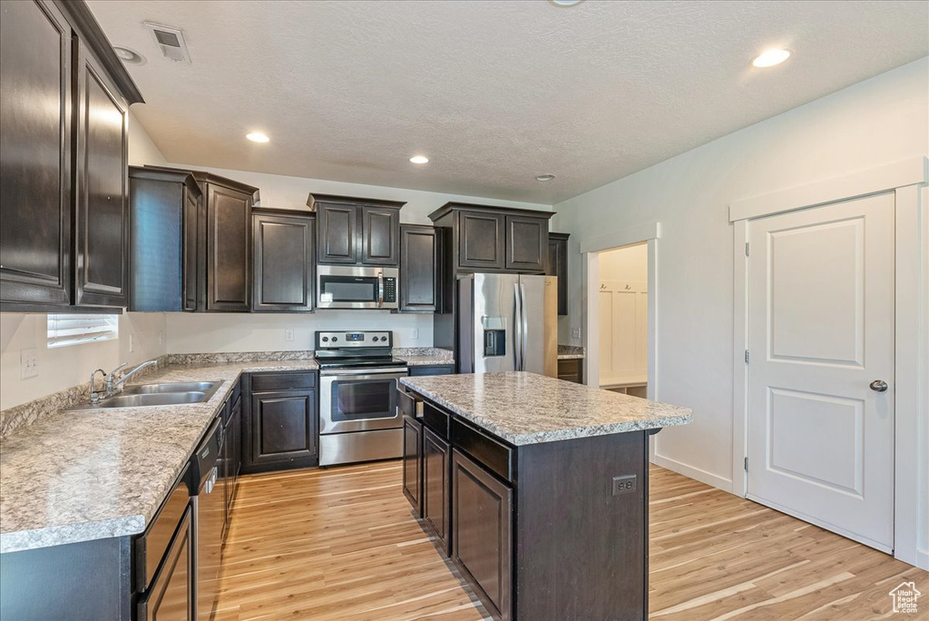 Kitchen with appliances with stainless steel finishes, light wood finished floors, a center island, light countertops, and recessed lighting