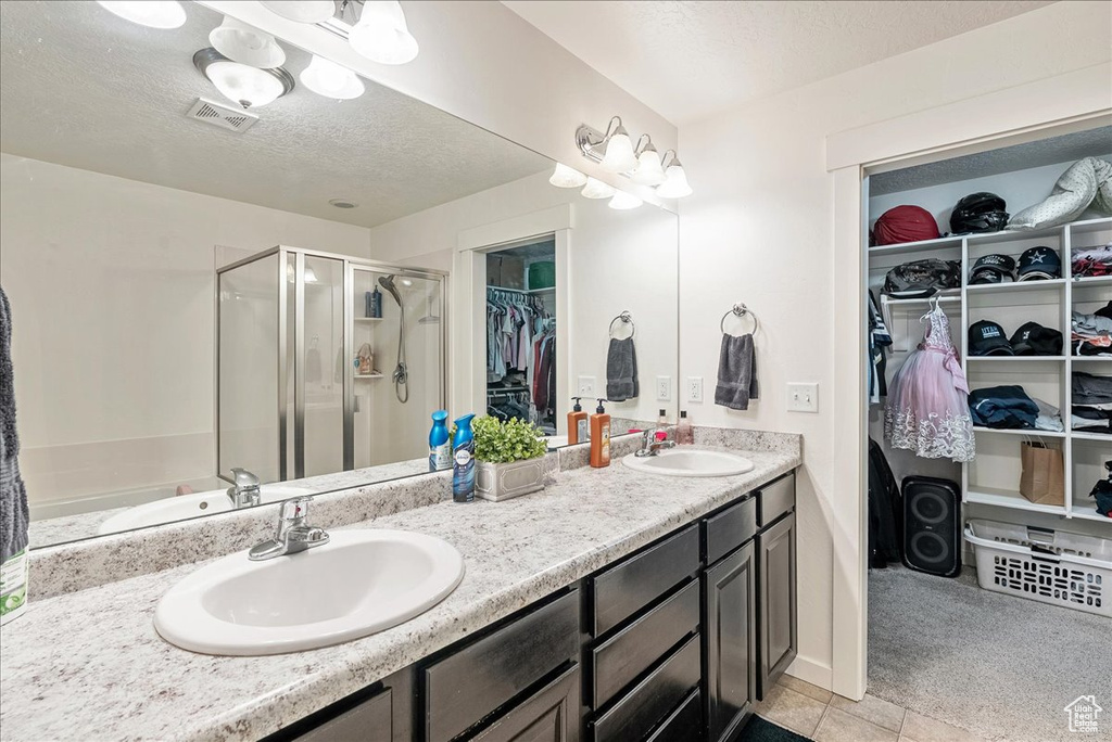 Full bathroom featuring a shower stall, double vanity, a spacious closet, a textured ceiling, and tile patterned flooring