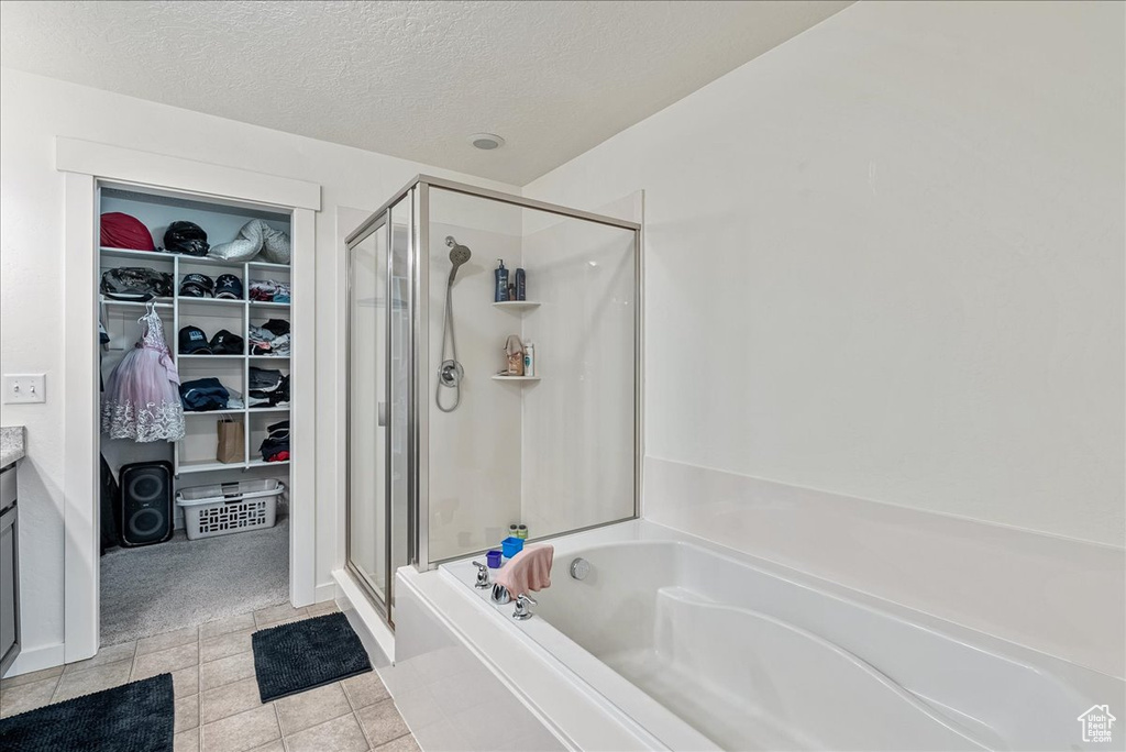 Full bath with a stall shower, a garden tub, a spacious closet, a textured ceiling, and vanity