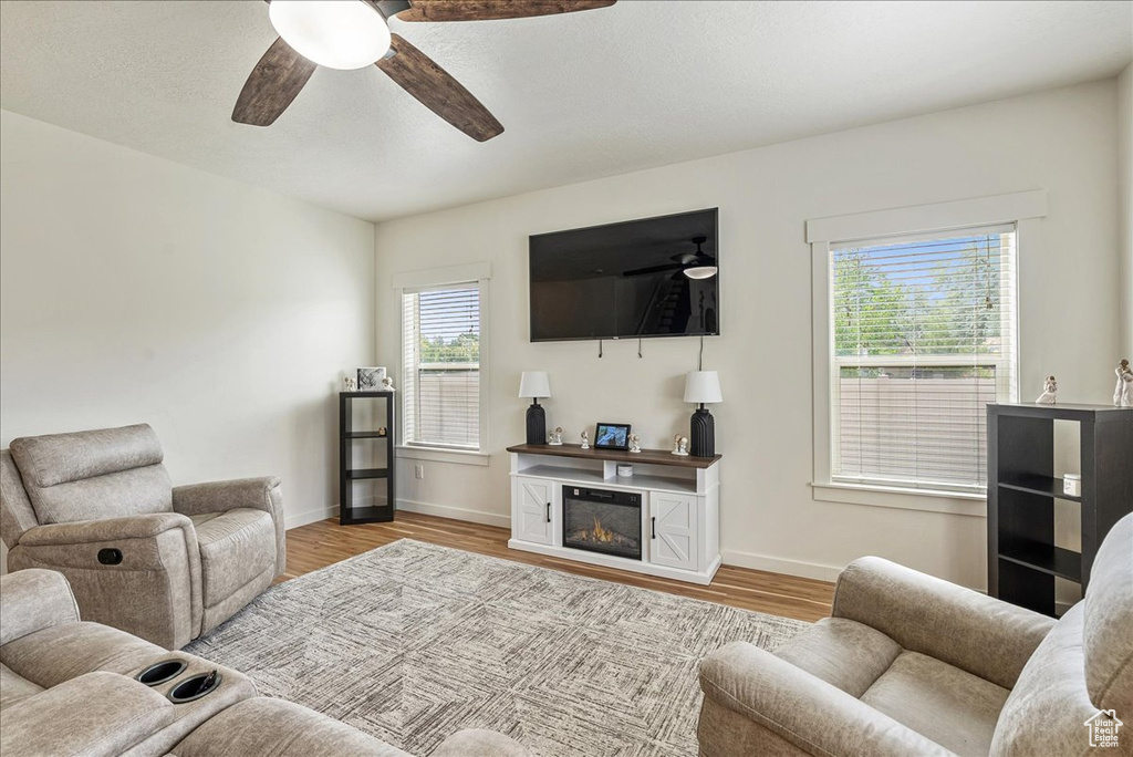 Living area with ceiling fan, wood finished floors, and a glass covered fireplace