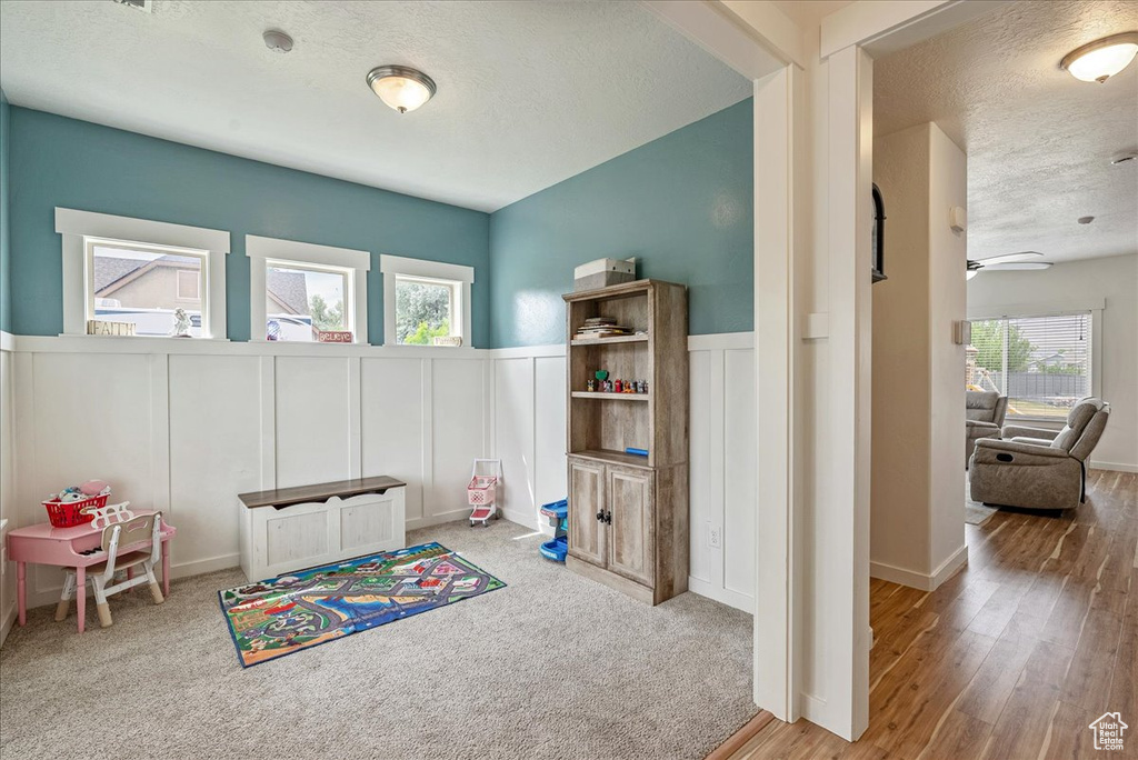 Playroom with a textured ceiling, a decorative wall, wainscoting, wood finished floors, and a ceiling fan