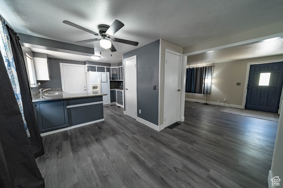 Kitchen featuring white refrigerator with ice dispenser, ceiling fan, a peninsula, dark wood-style flooring, and a textured ceiling