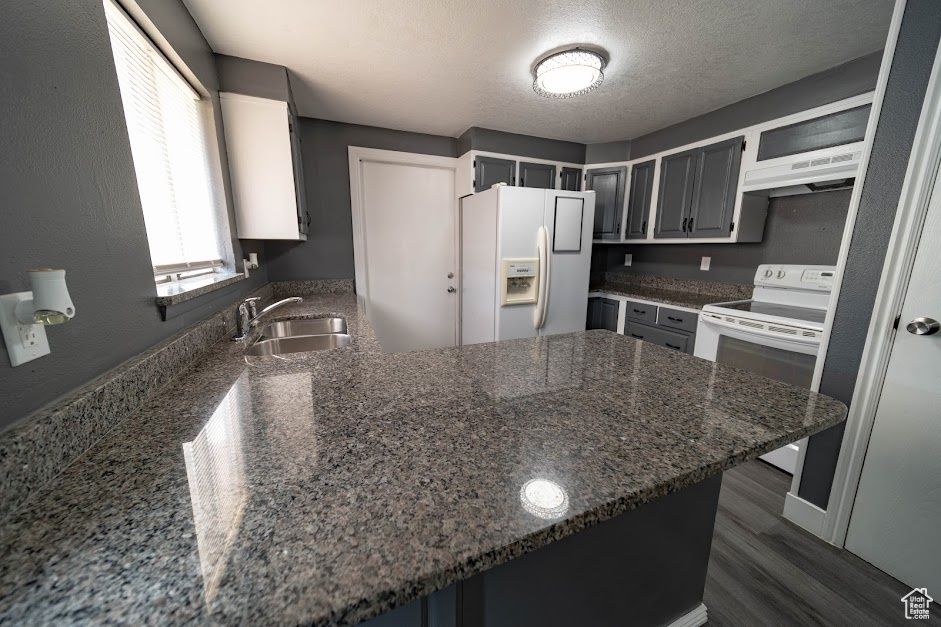 Kitchen featuring white appliances, a peninsula, ventilation hood, dark stone countertops, and dark wood-style flooring