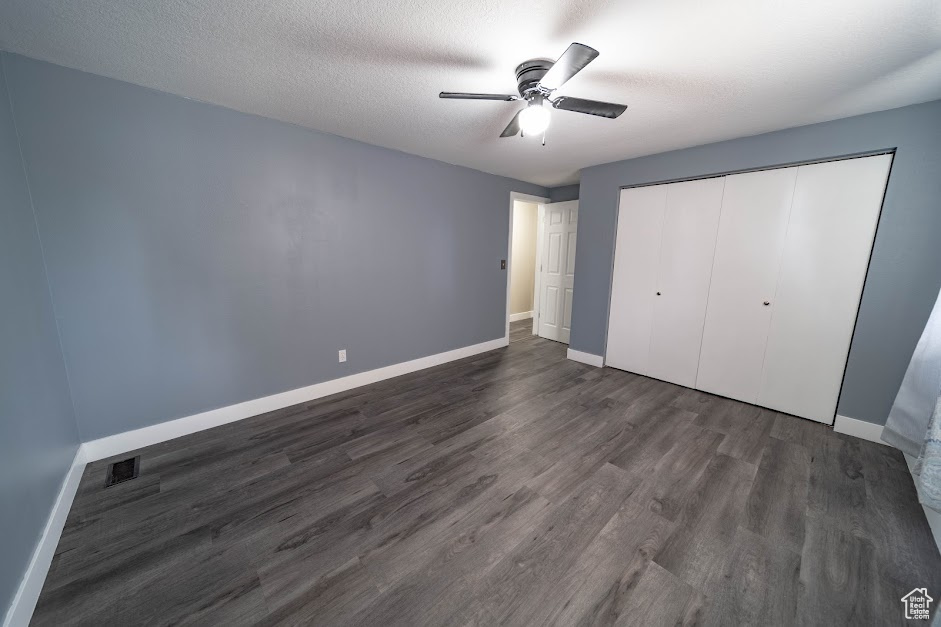 Unfurnished bedroom with dark wood-type flooring, a closet, ceiling fan, and a textured ceiling