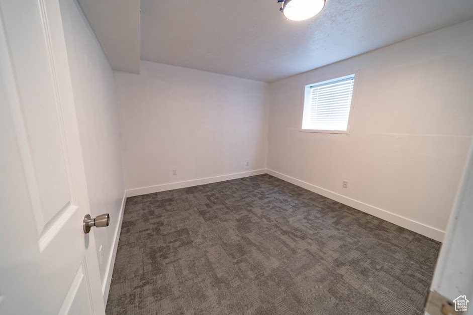 Empty room with baseboards and dark carpet