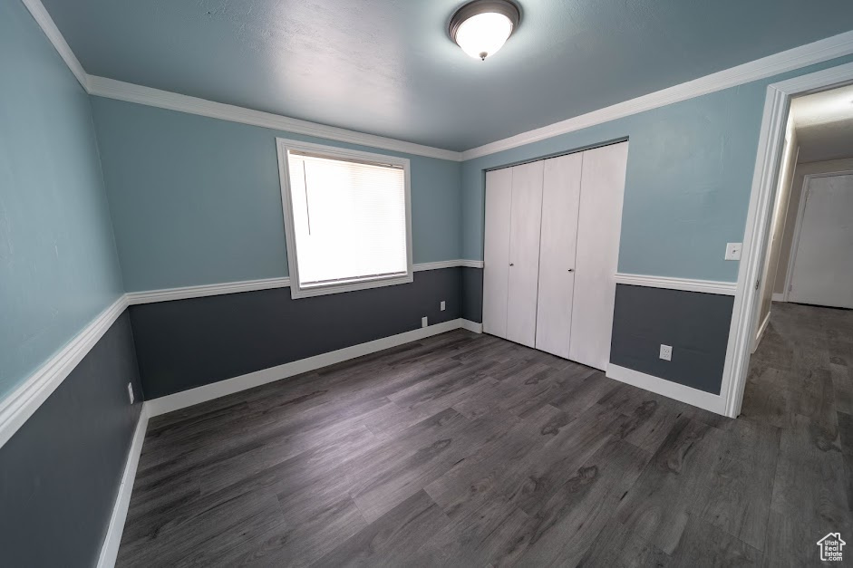 Unfurnished bedroom featuring wood finished floors, a closet, and crown molding