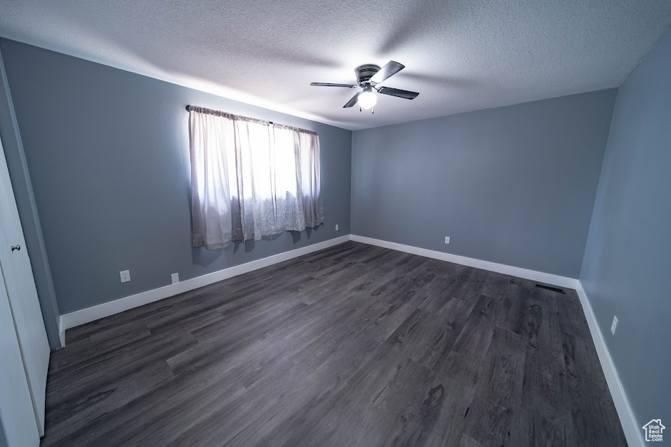 Empty room with a textured ceiling, ceiling fan, and dark wood-style flooring