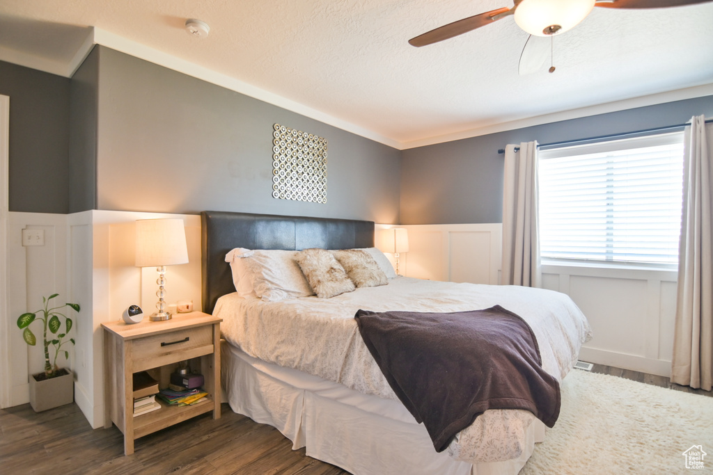 Bedroom featuring a wainscoted wall, wood finished floors, ceiling fan, and a decorative wall