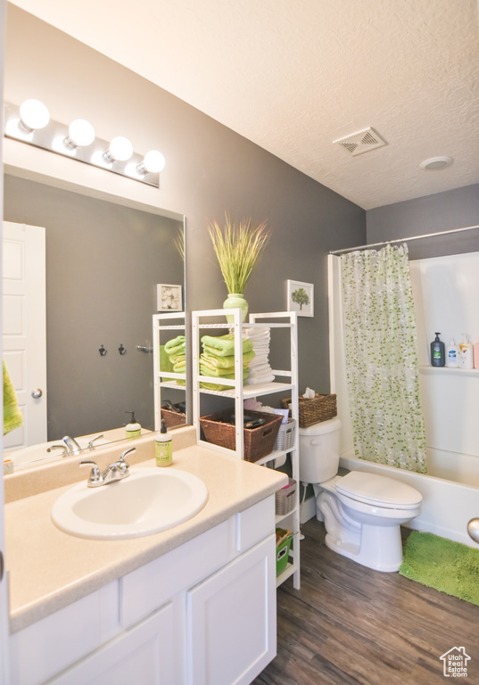 Full bath featuring vanity, wood finished floors, shower / tub combo with curtain, and a textured ceiling