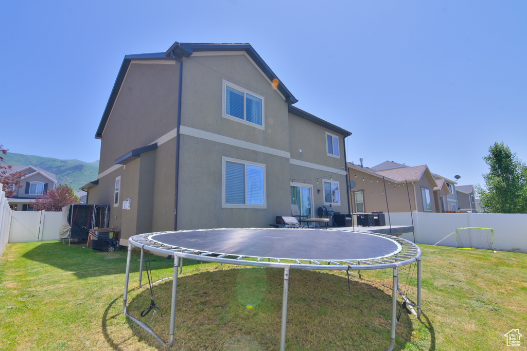 Rear view of property featuring a trampoline, a fenced backyard, stucco siding, and a gate