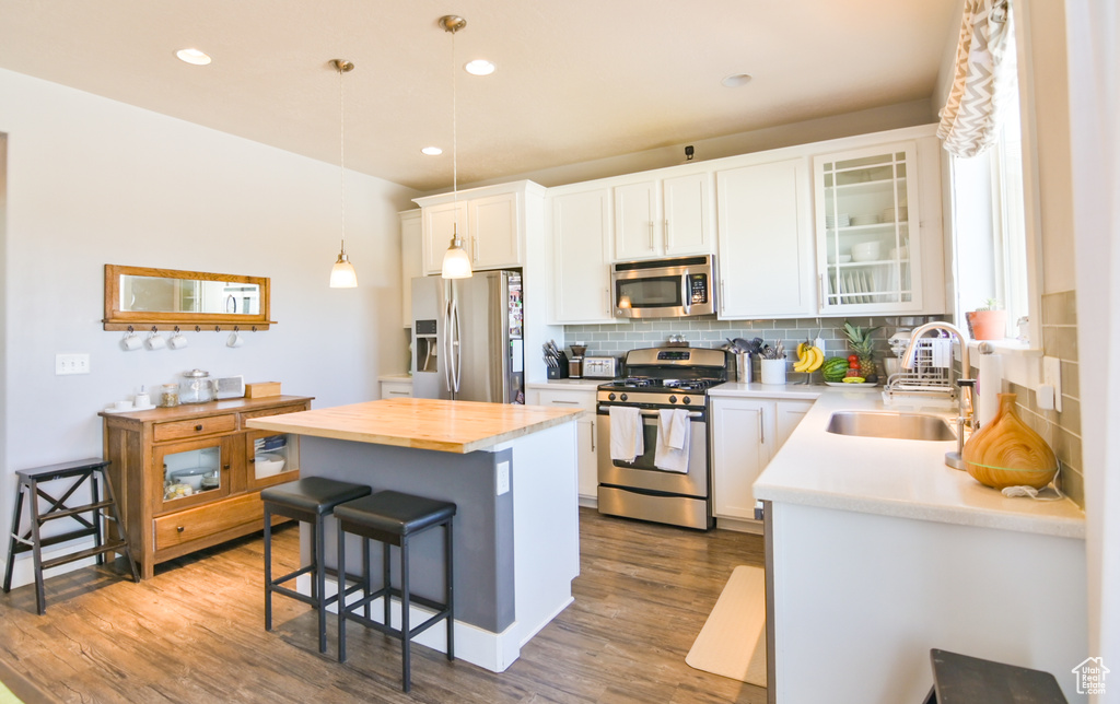 Kitchen with stainless steel appliances, a breakfast bar, decorative backsplash, a center island, and dark wood-type flooring