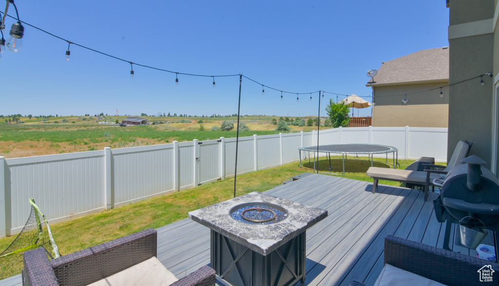 Deck with a trampoline, a fenced backyard, a fire pit, and area for grilling