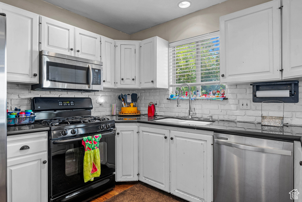 Kitchen with stainless steel appliances, dark countertops, white cabinets, and backsplash
