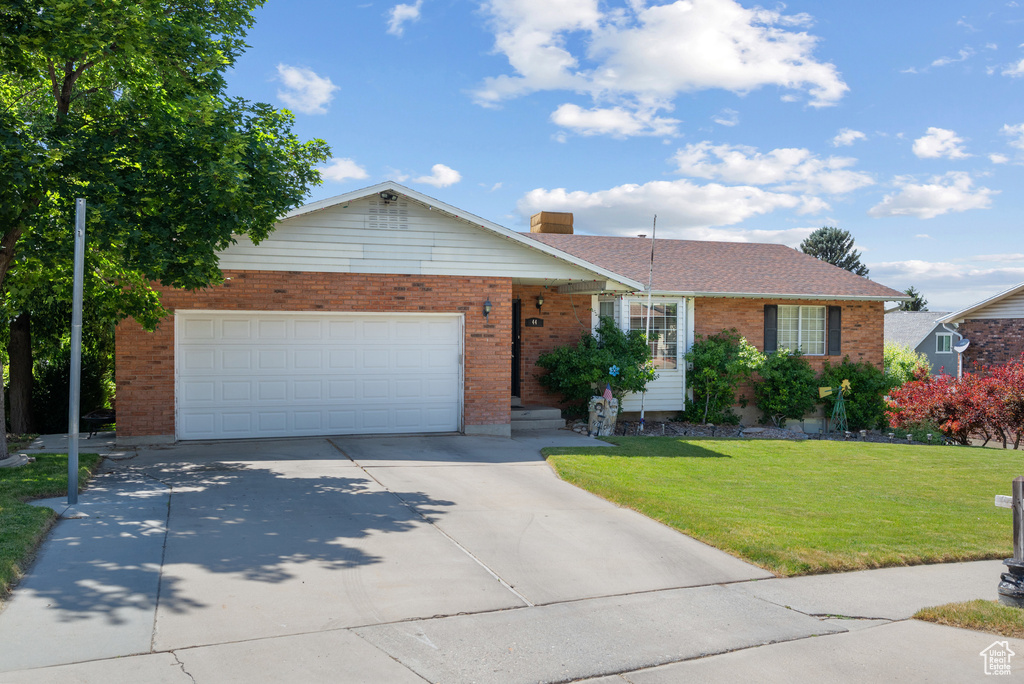 Single story home with brick siding, driveway, a front lawn, an attached garage, and a chimney