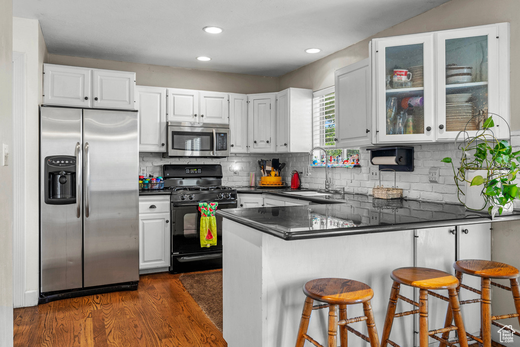 Kitchen with stainless steel appliances, dark countertops, a peninsula, dark wood-style flooring, and recessed lighting