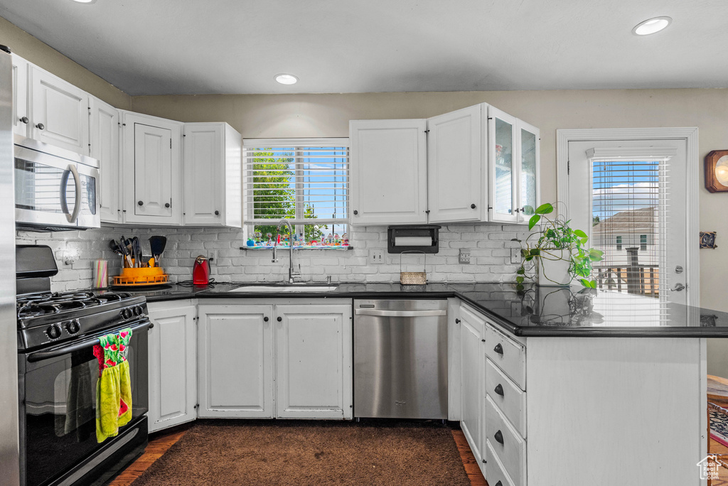 Kitchen with stainless steel appliances, dark countertops, white cabinets, a peninsula, and recessed lighting