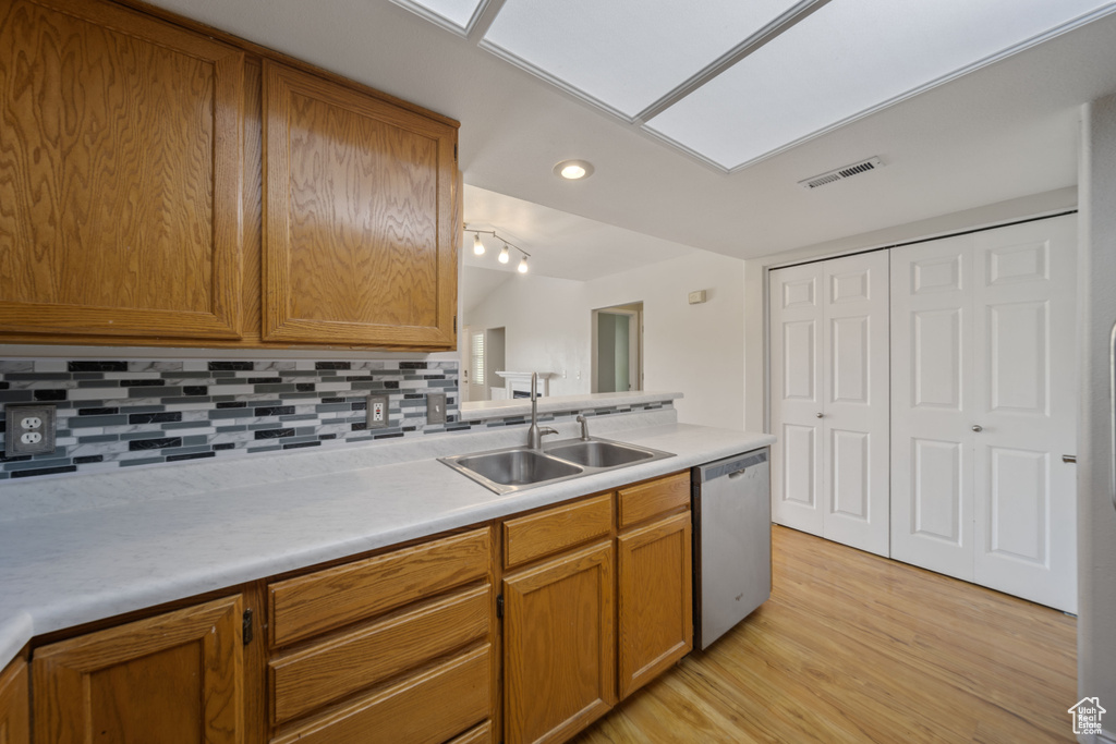 Kitchen featuring stainless steel dishwasher, decorative backsplash, brown cabinetry, light wood finished floors, and light countertops
