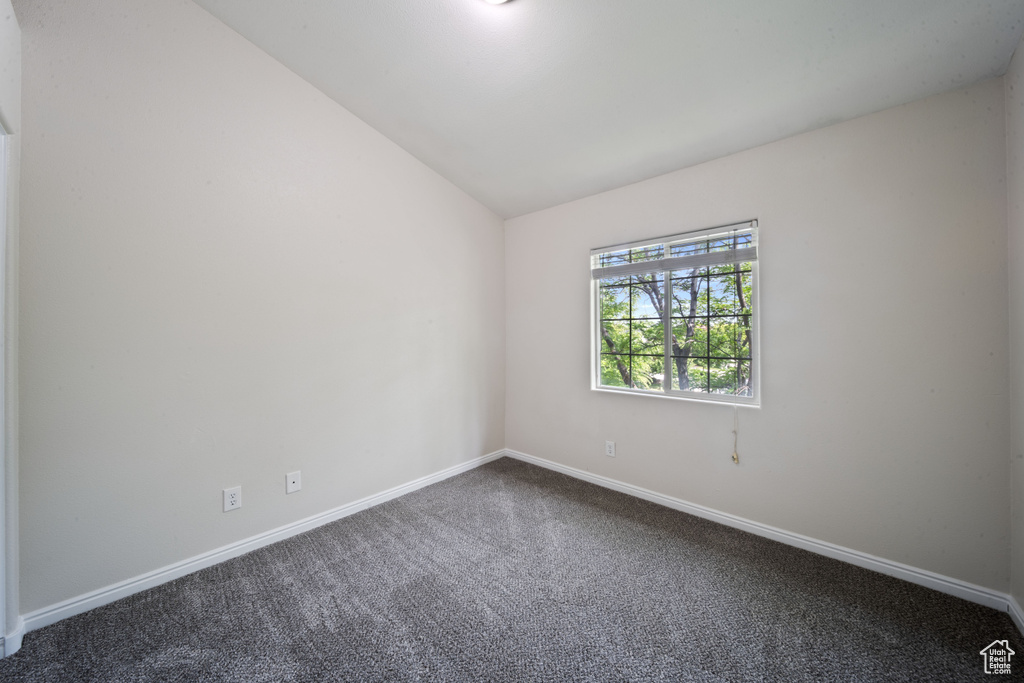 Spare room featuring dark colored carpet and lofted ceiling