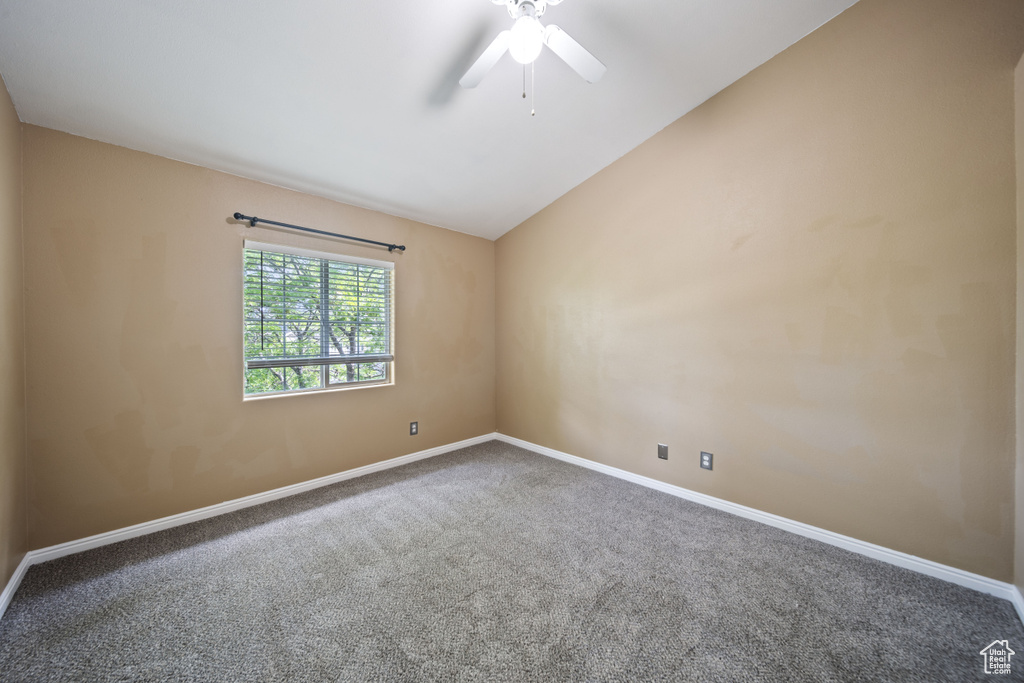 Carpeted spare room featuring vaulted ceiling and ceiling fan