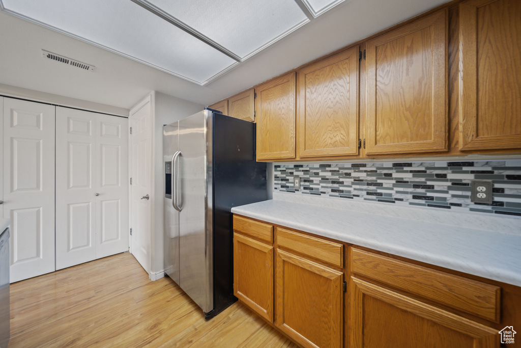 Kitchen with stainless steel fridge with ice dispenser, light wood-type flooring, light countertops, backsplash, and brown cabinetry