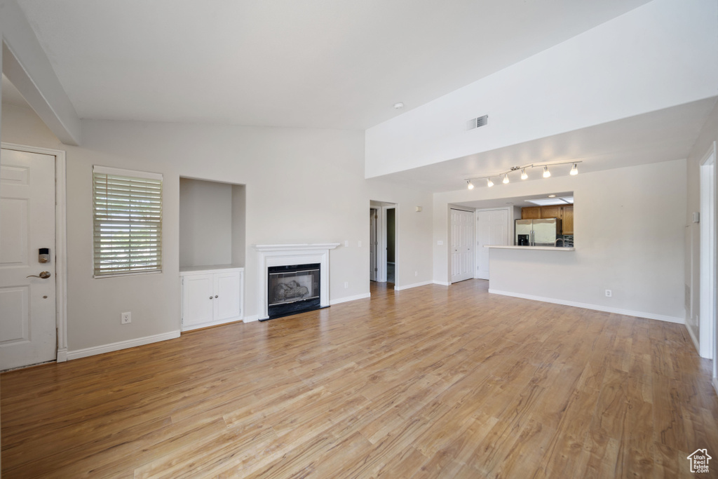 Unfurnished living room featuring a glass covered fireplace, vaulted ceiling, light wood-type flooring, and rail lighting