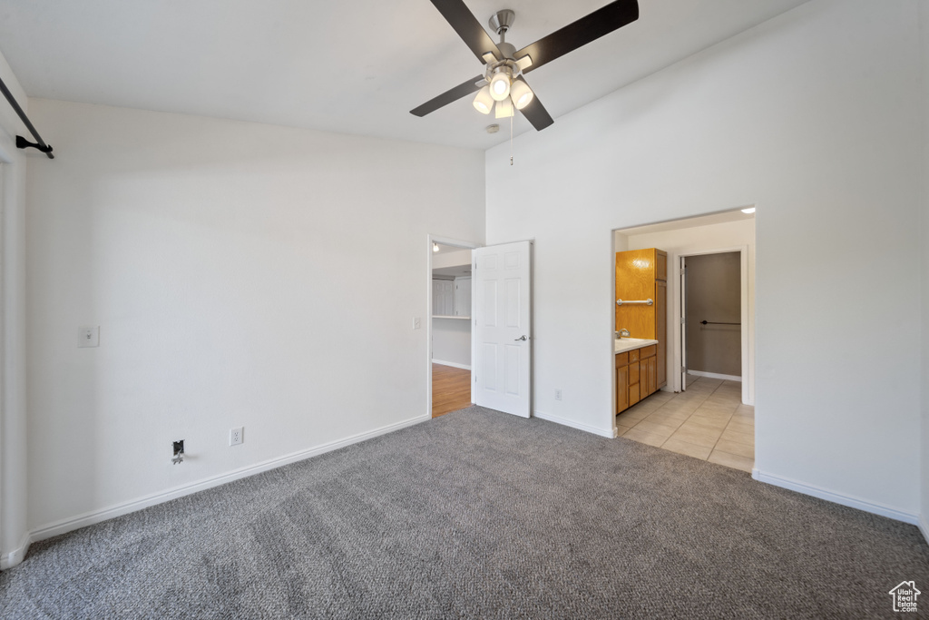 Unfurnished bedroom featuring light carpet, high vaulted ceiling, ensuite bathroom, a walk in closet, and light tile patterned floors