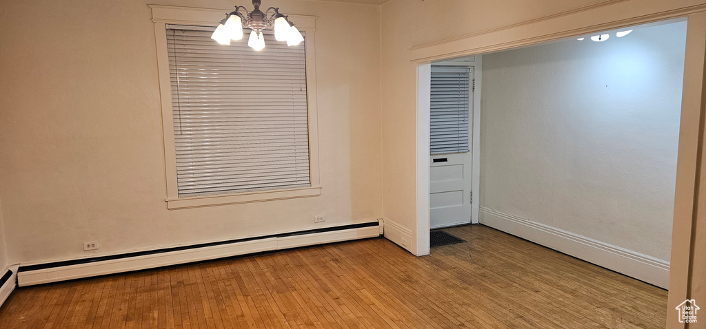 Empty room with a baseboard heating unit, a chandelier, and wood finished floors