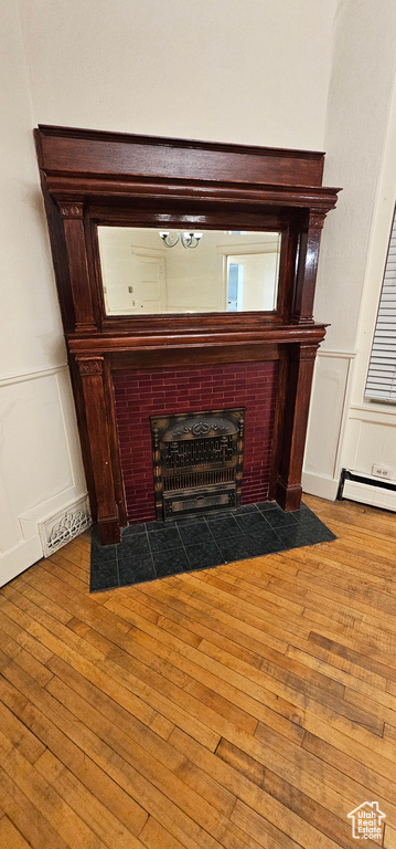 Detailed view of a brick fireplace, a decorative wall, wood finished floors, wainscoting, and baseboard heating