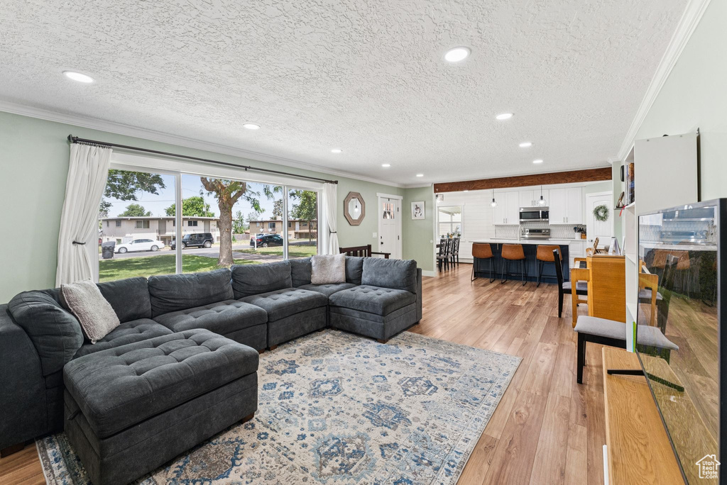 Living room featuring crown molding, a textured ceiling, light wood-style flooring, and recessed lighting