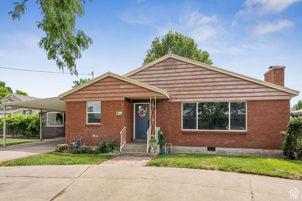View of front of home featuring a chimney, concrete driveway, an attached carport, and brick siding