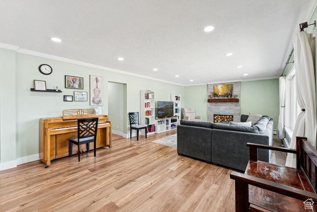 Living area with light wood finished floors, recessed lighting, a fireplace, a textured ceiling, and ornamental molding