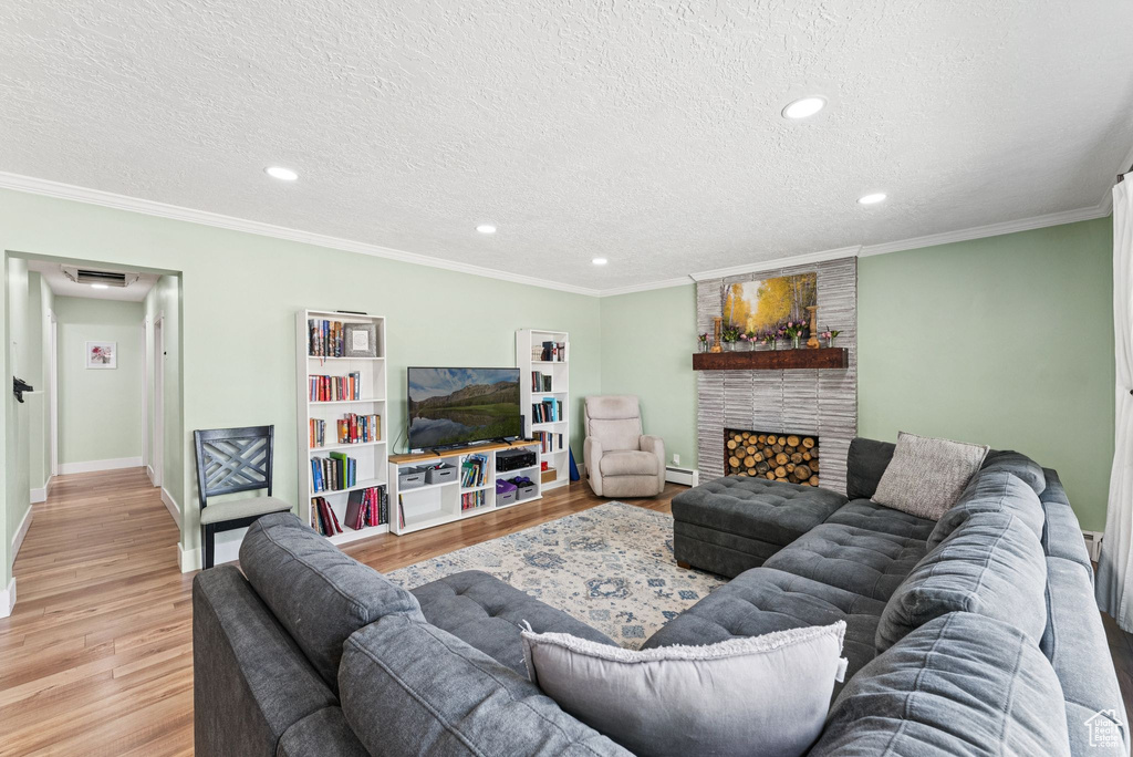 Living room with light wood-style floors, a textured ceiling, a baseboard heating unit, recessed lighting, and a fireplace