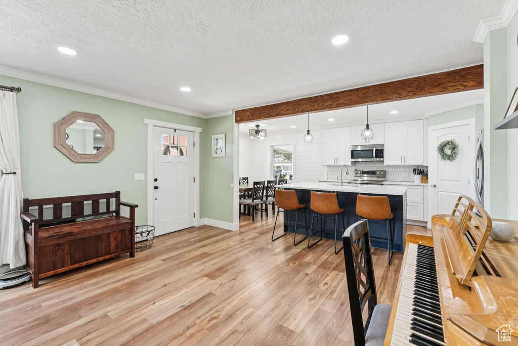 Living area featuring a textured ceiling, light wood-style floors, ornamental molding, and recessed lighting