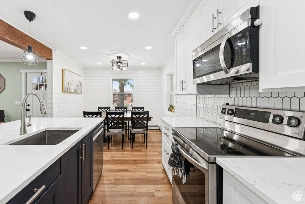Kitchen with appliances with stainless steel finishes, light wood finished floors, white cabinetry, ornamental molding, and pendant lighting