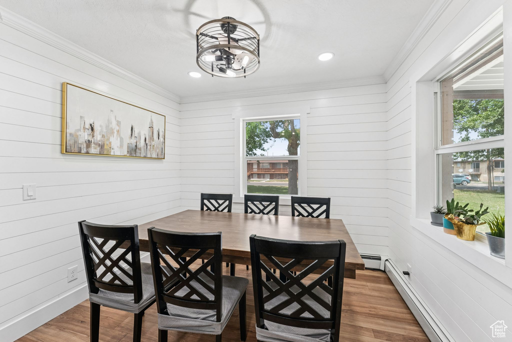 Dining area featuring baseboard heating, ornamental molding, wood finished floors, a chandelier, and wooden walls