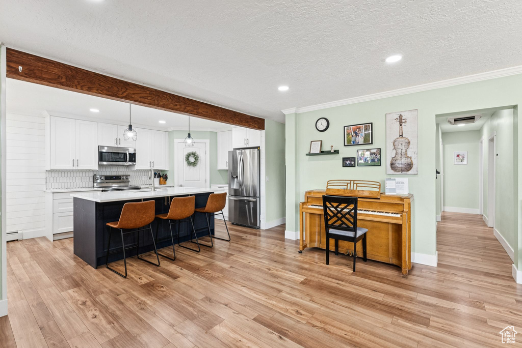 Kitchen featuring appliances with stainless steel finishes, a breakfast bar, light countertops, a textured ceiling, and white cabinets