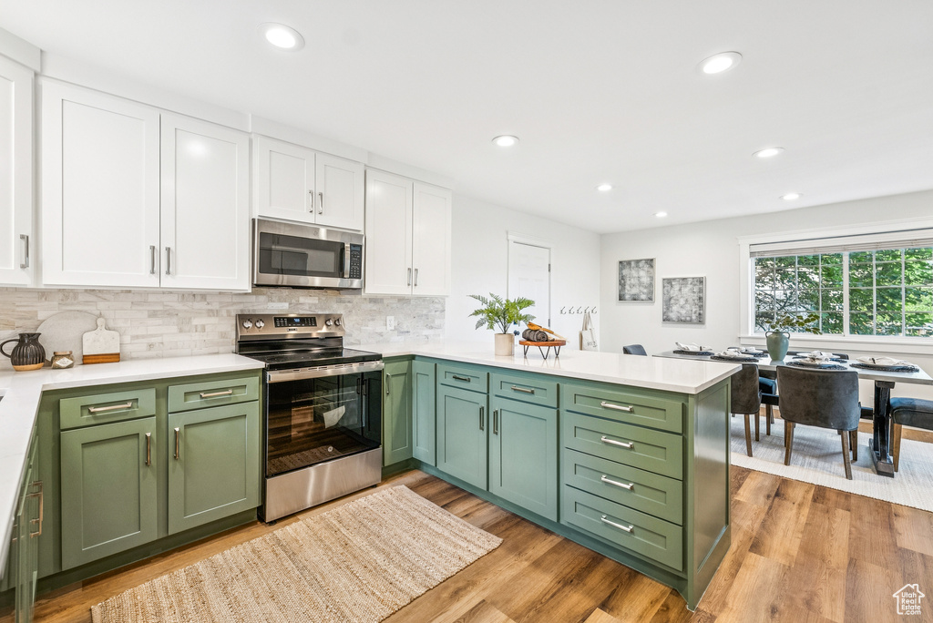 Kitchen featuring appliances with stainless steel finishes, green cabinetry, white cabinetry, light countertops, and recessed lighting