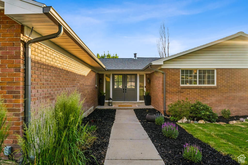 Doorway to property featuring brick siding, french doors, and a shingled roof