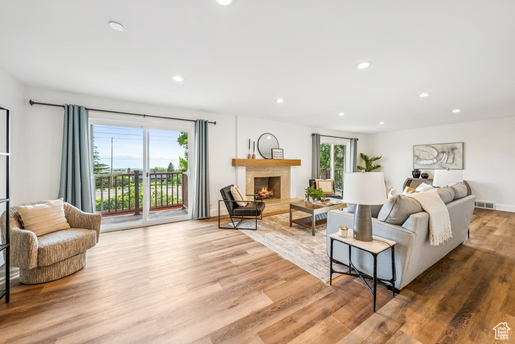 Living area with wood finished floors, a warm lit fireplace, and recessed lighting