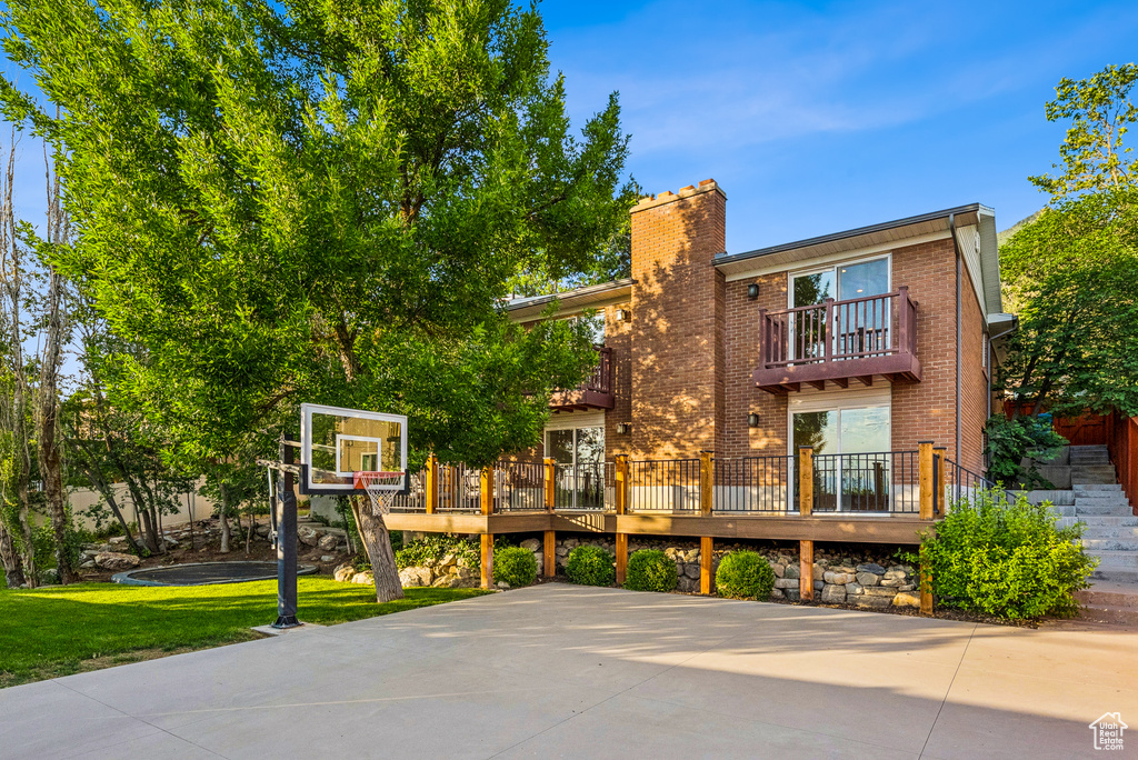 Back of property featuring a balcony, brick siding, a chimney, a lawn, and basketball court