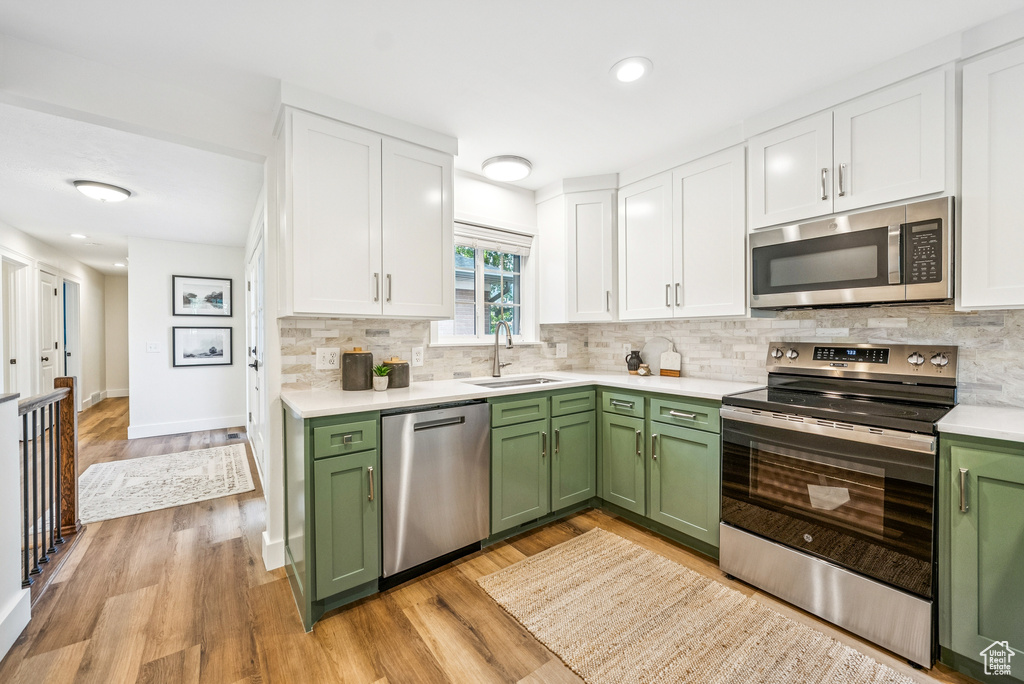 Kitchen with green cabinetry, appliances with stainless steel finishes, white cabinetry, light countertops, and decorative backsplash