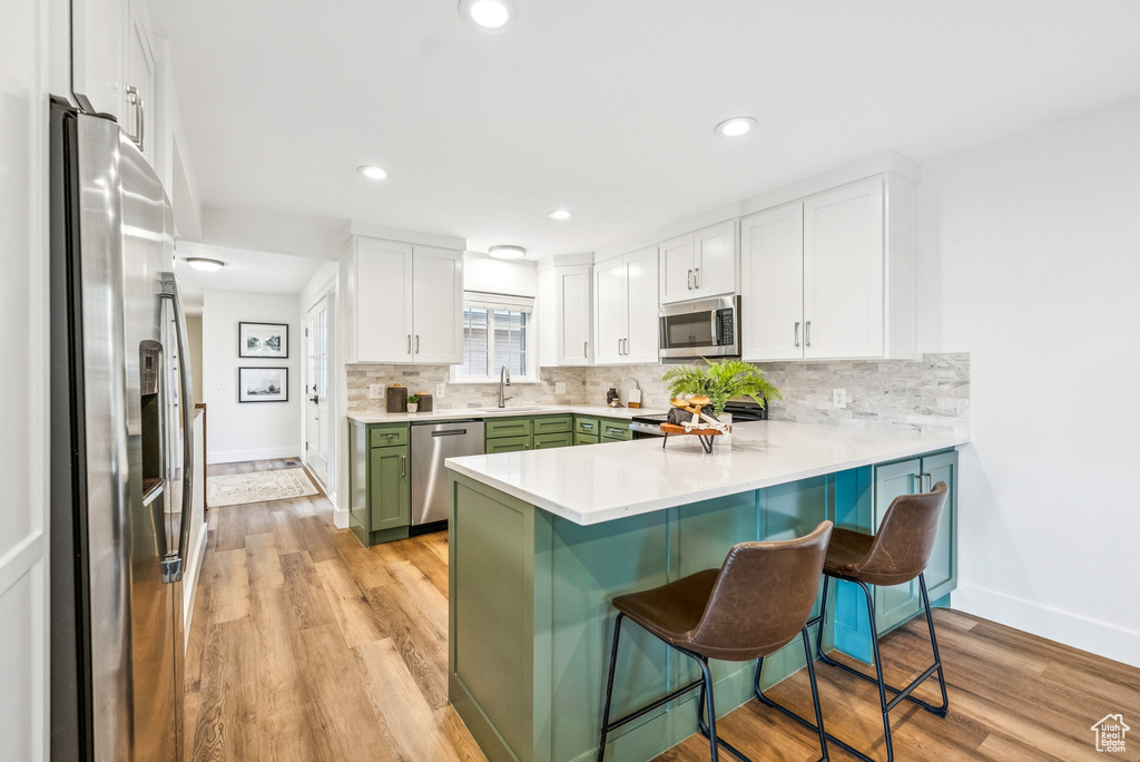 Kitchen with stainless steel appliances, green cabinetry, a peninsula, a kitchen bar, and white cabinets