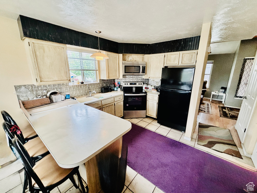Kitchen featuring stainless steel appliances, light tile patterned floors, decorative backsplash, a peninsula, and light countertops