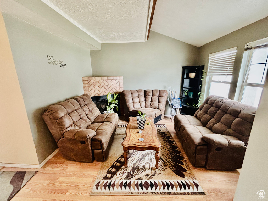 Living room featuring wood finished floors, lofted ceiling, a tiled fireplace, a textured ceiling, and ornamental molding